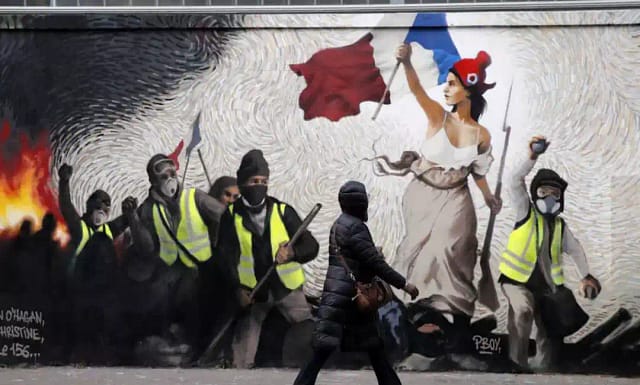 Una mujer pasa junto a un mural del artista callejero PBOY que representa a manifestantes de los chalecos amarillos (gilets jaunes) inspirados en una pintura de Eugene Delacroix, "La Liberté guidant le Peuple" (La libertad guiando al pueblo), en París, el jueves 10 de enero de 2019. AP - Christophe Ena